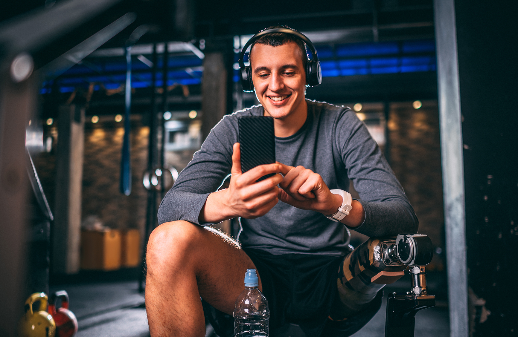 Young adaptive male athlete using a mobile phone while listening to music in a gym arena of a gym.